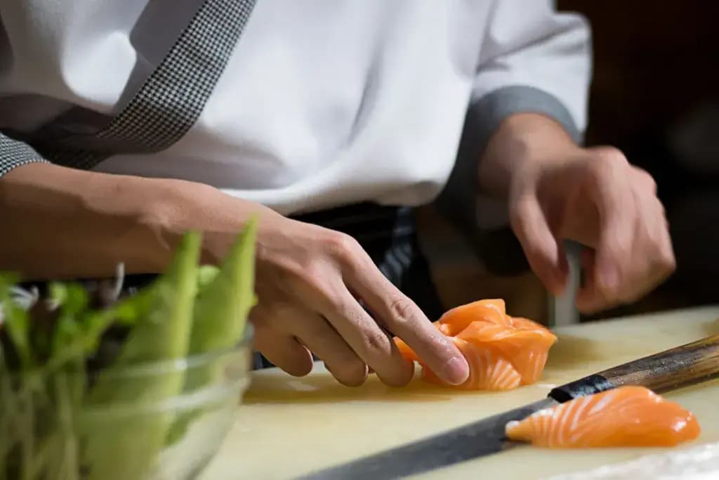 A person using a Japanese garnish knife to create a sashimi salmon rose.