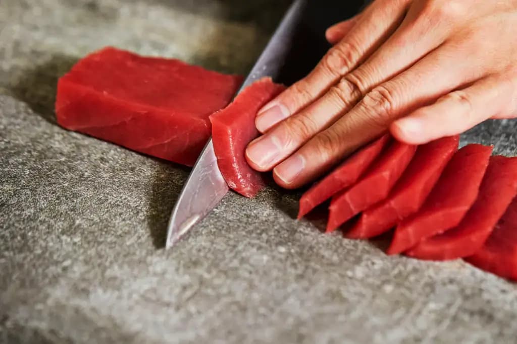A person slicing tuna sashimi.