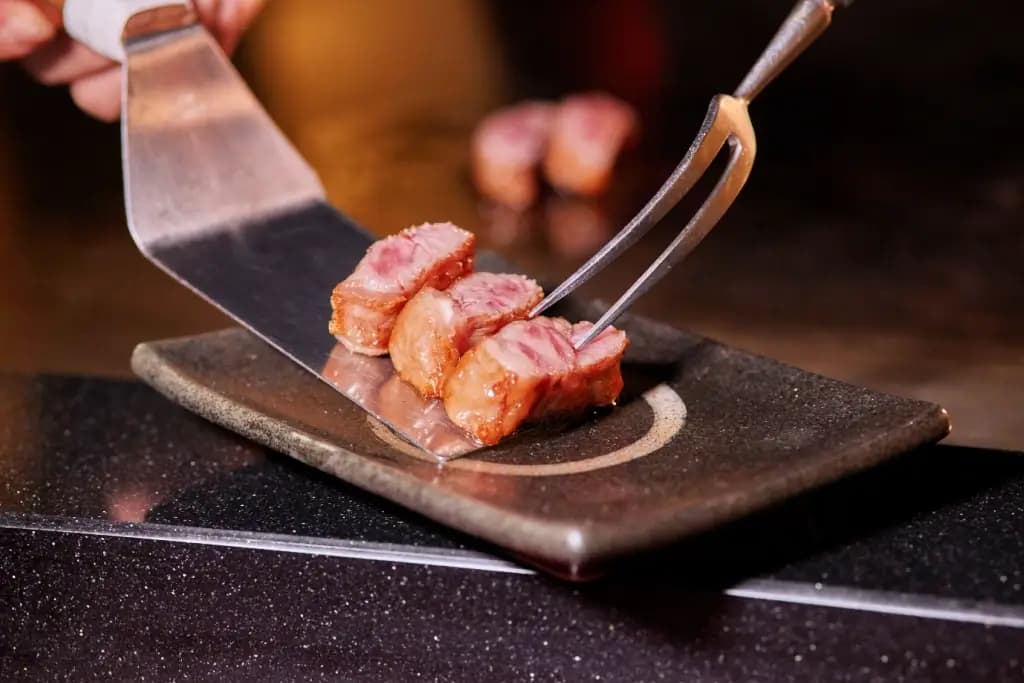 A chef placing steak on a plate in a steakhouse.