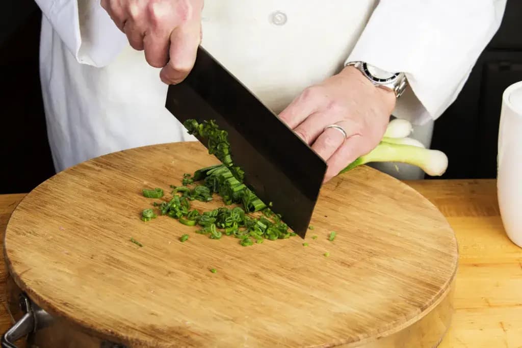 A person using a chukabocho to chop up scallions.